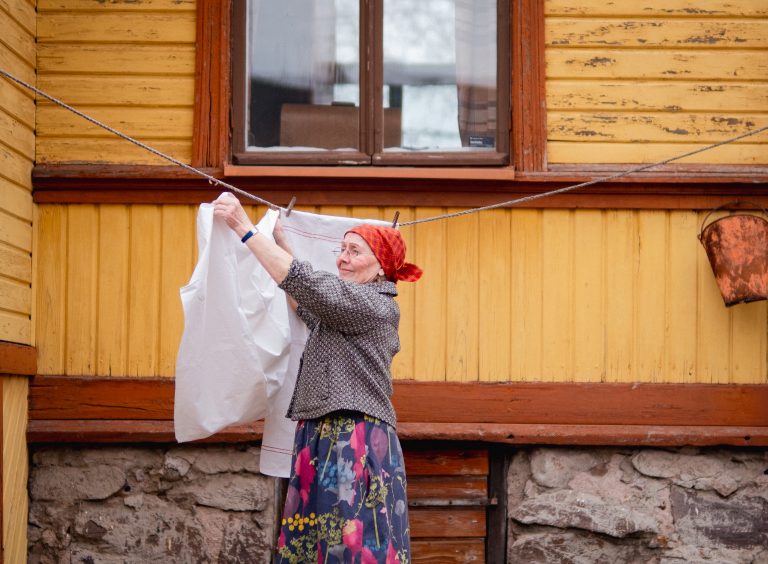 Vanhanajan pyykkärihahmo ripustaa pyykkiä narulle.