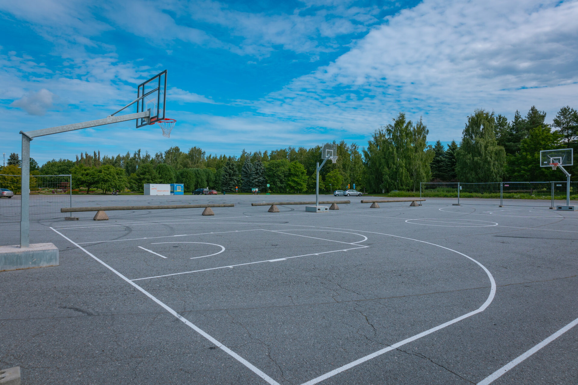 edustalla koripallokenttä, taustalla parkkipaikka jossa autoja sekä puita