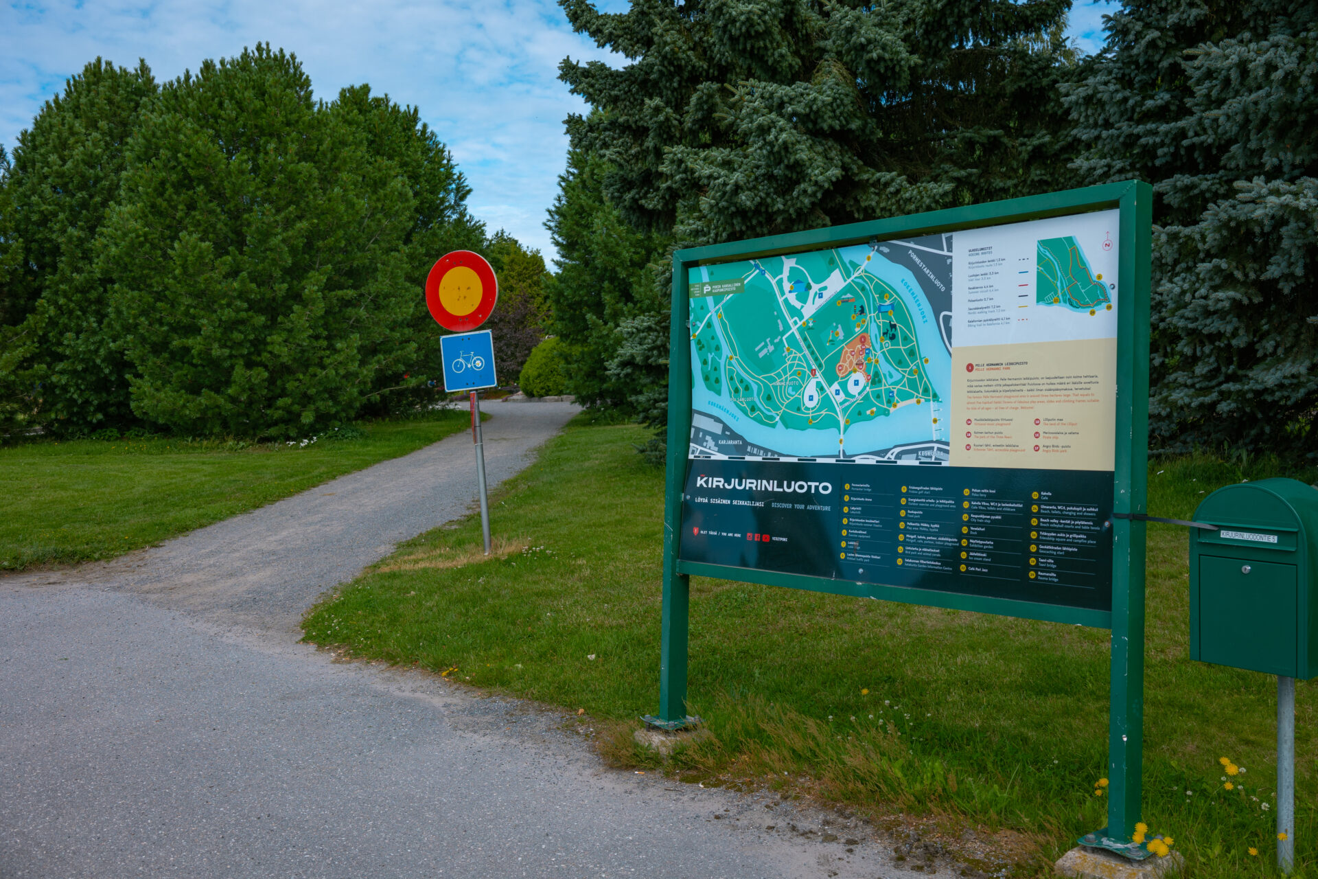 opastekyltti jonka vieressä sorapolku ja liikennemerkki, taustalla puita