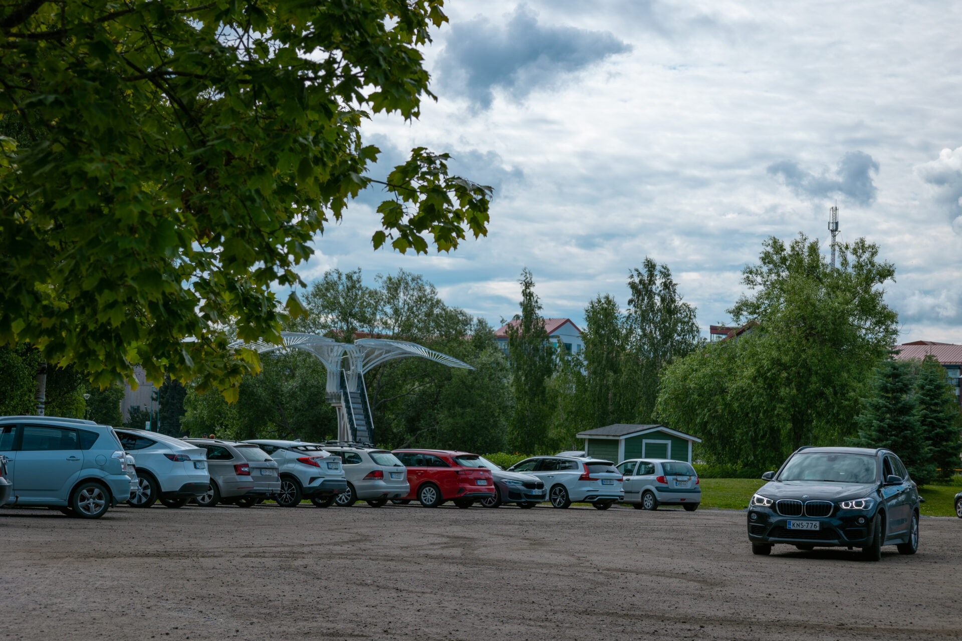 parkkipaikka jossa autoja, taustalla muistomerkki