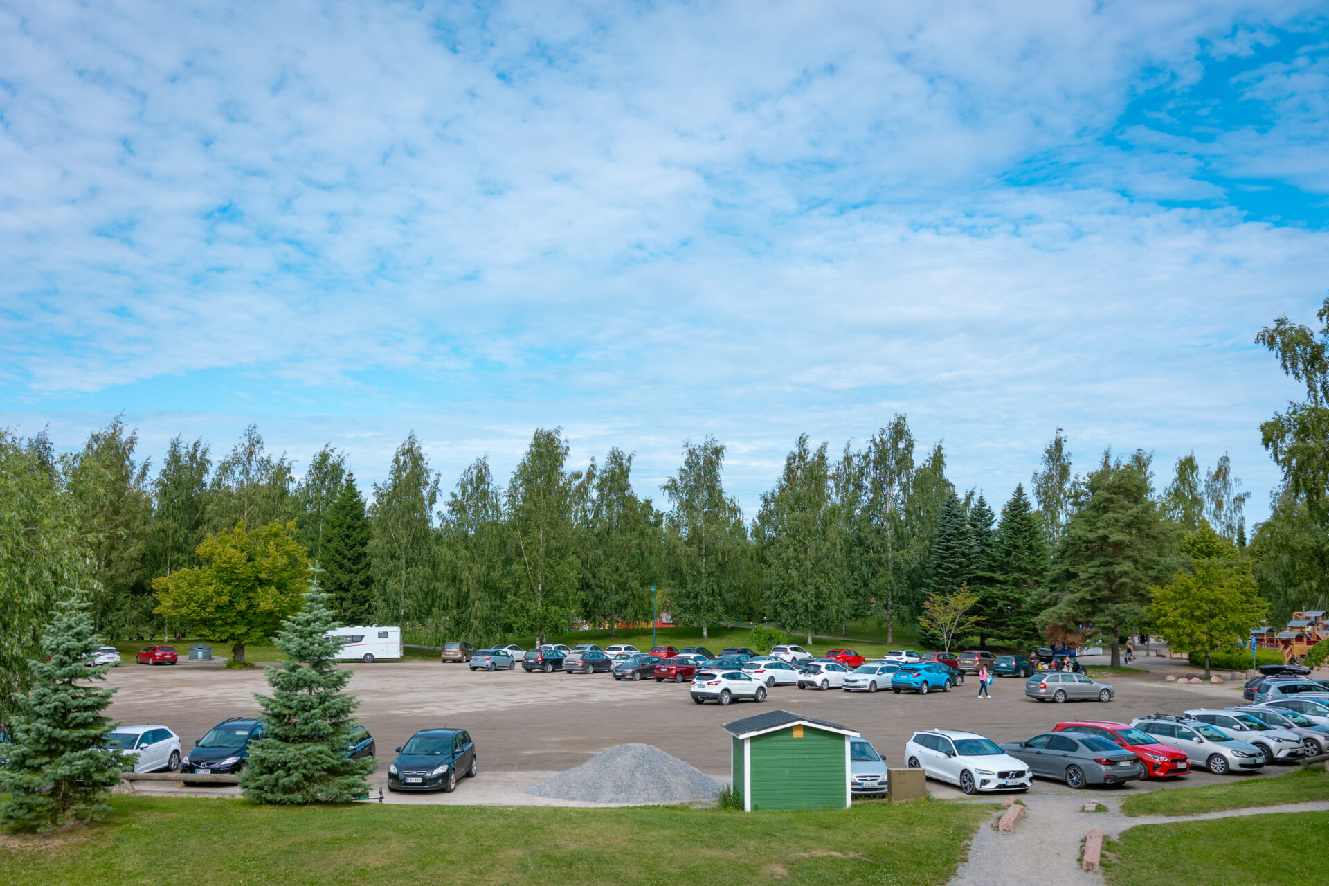 parkkipaikka jossa autoja, taustalla puita