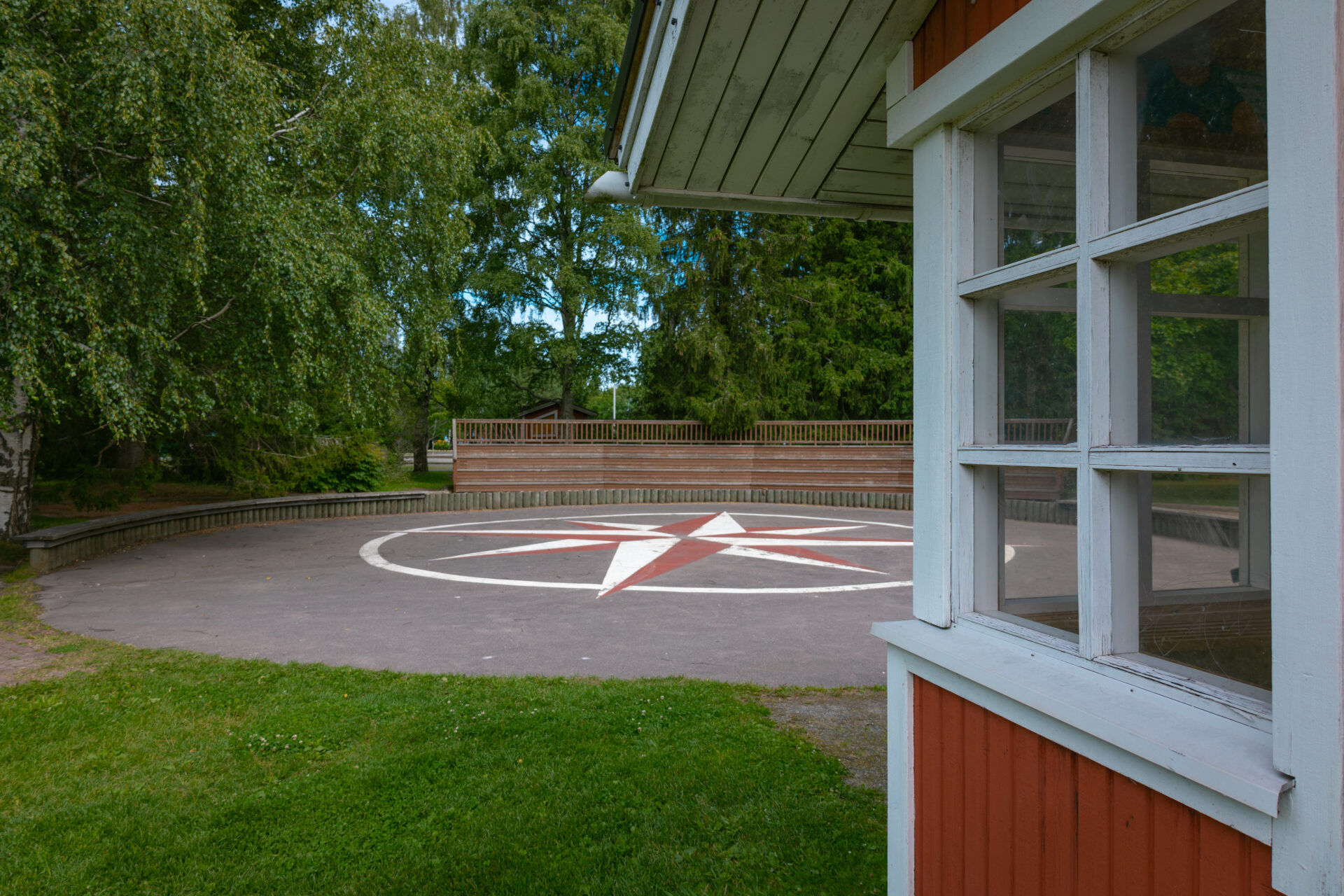 esiintymisalue, taustalla katsomo ja puita, edustalla punainen rakennus jossa valkoiset ikkunapokat