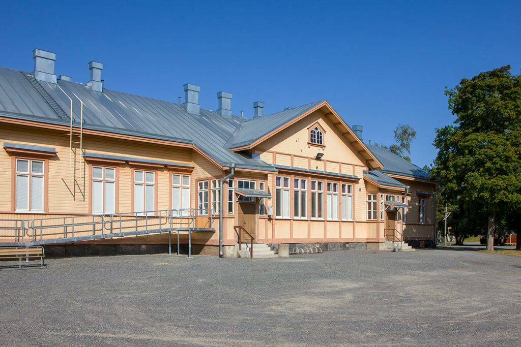 puinen rakennus jossa kaksi ulko-ovea, toisen oven vieressä pyörätuoliluiska