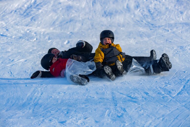 Nainen ja kaksi lasta nauravat laskiessaan pulkkamäessä Yyterissä