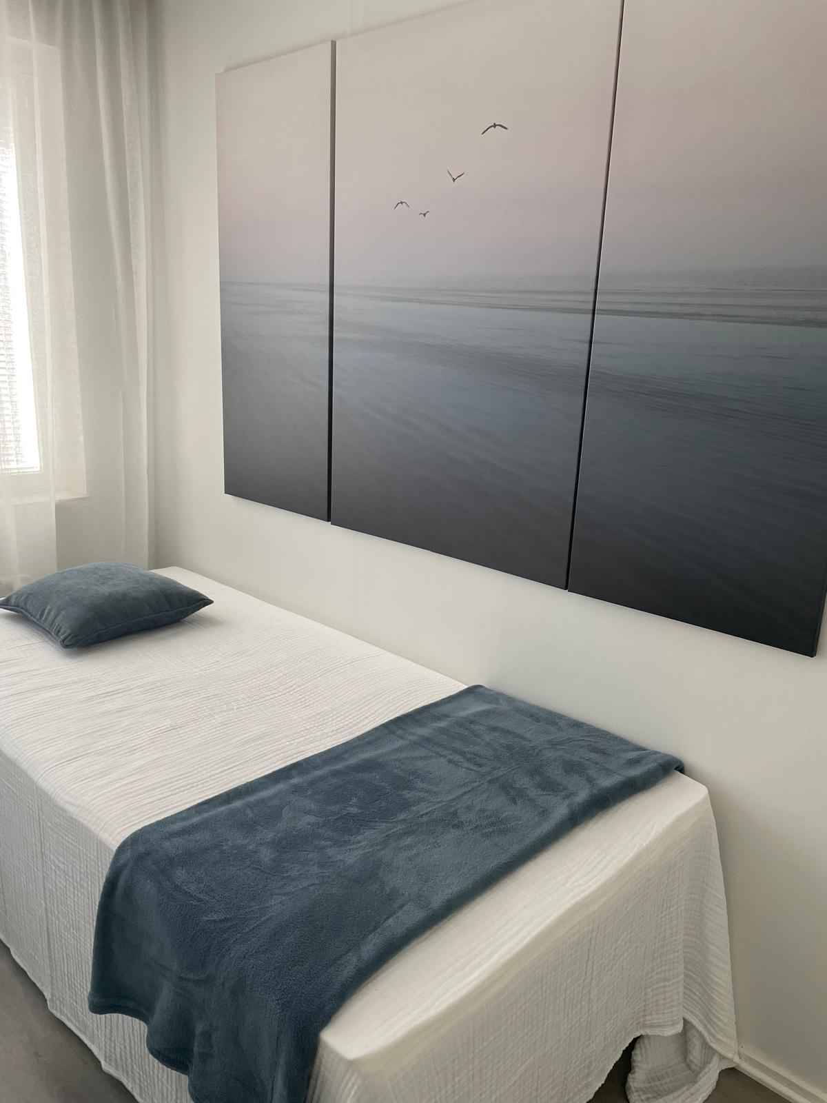Loma-asunto Beach House Yyterin makuuhuoneen yksittäinen vuode ja merimaisemataulu seinällä