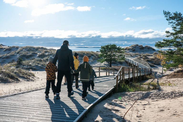 A family walking down a wooden boardwalk in front of sand dunes.