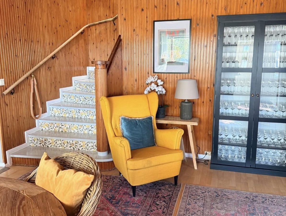 Villa Rouheen portaat yläkertaan. Tilassa keltainen nojatuoli ja lasikaappi.